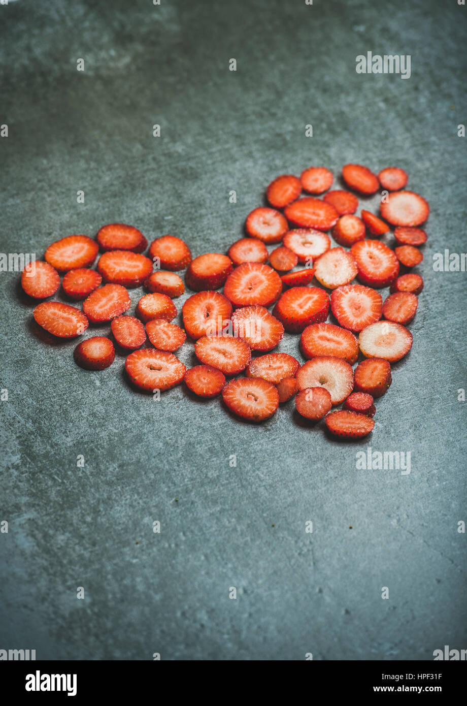 Pieces of fresh strawberries in shape of heart on grey concrete background, selective focus, copy space, vertical composition. Valentine's day food co Stock Photo