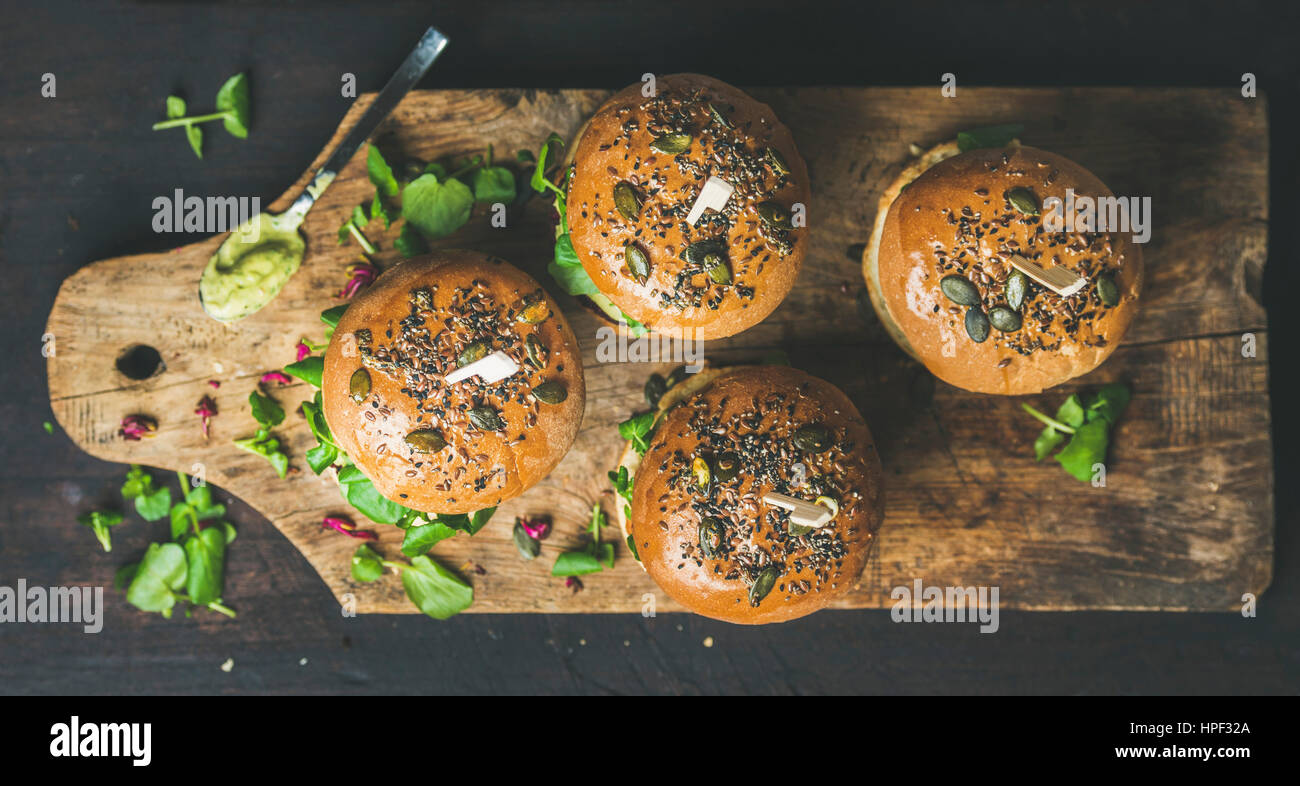Healthy vegan burger with beetroot and quinoa patty, arugula, avocado sauce, wholegrain bun on rustic wooden board over dark wooden background, top vi Stock Photo