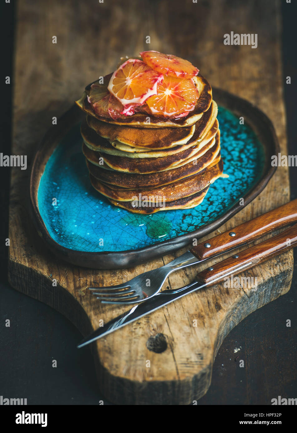 Homemade pancakes with honey and bloody orange slices for breakfast on blue ceramic plate over rustic wooden board, dark wooden scorched background, s Stock Photo