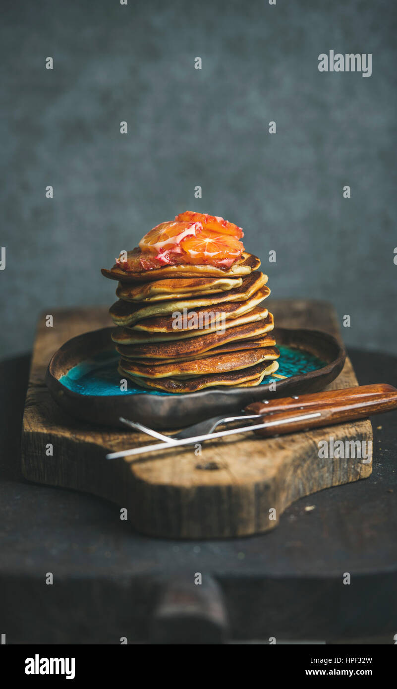 Homemade pancakes with honey and bloody orange slices for breakfast on blue ceramic plate over rustic wooden board, grey plywood wall at background, s Stock Photo