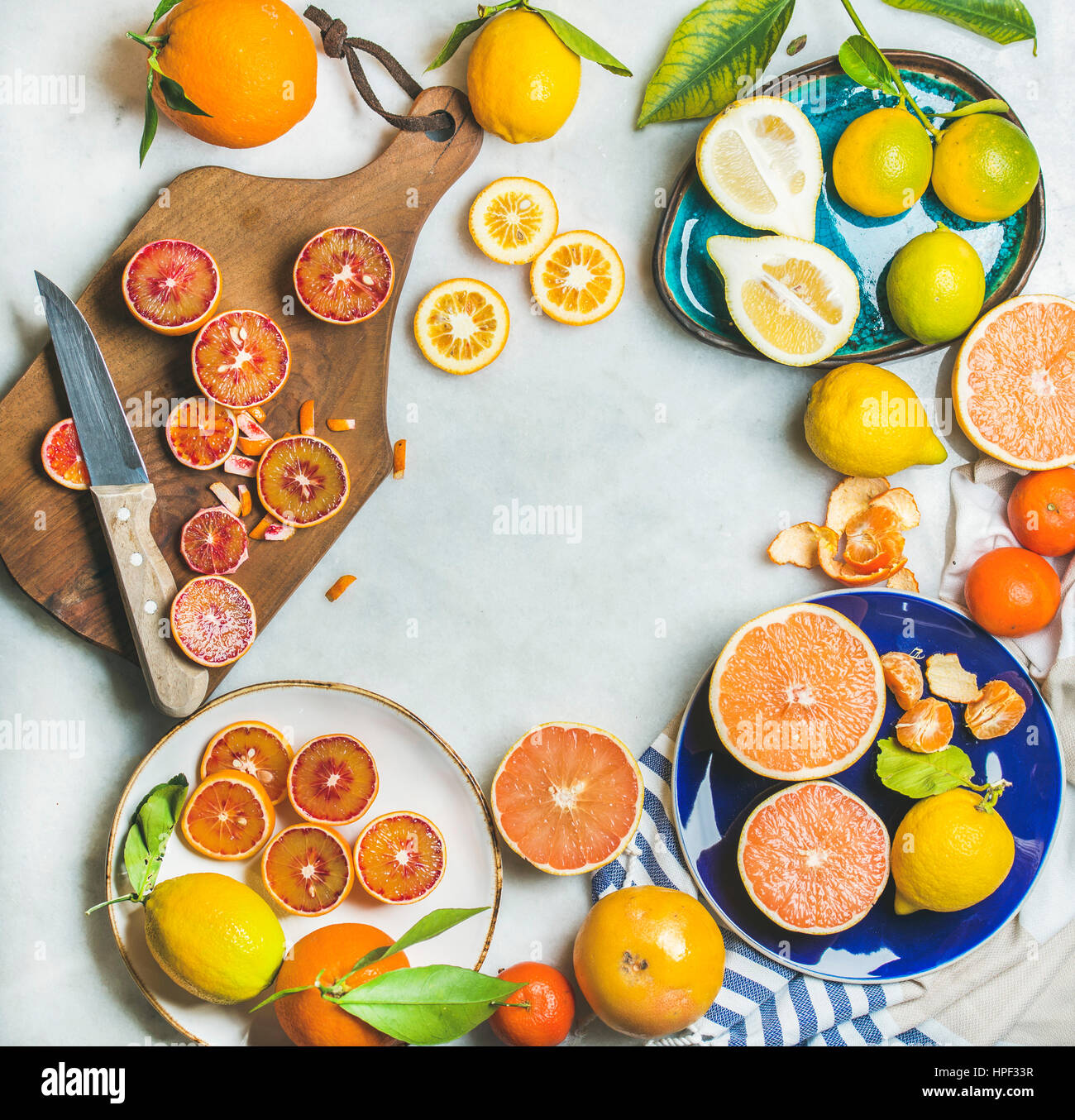 Natural fresh citrus fruits on wooden rustic board, colorful ceramic plates over grey marble table background, top view, copy space Stock Photo