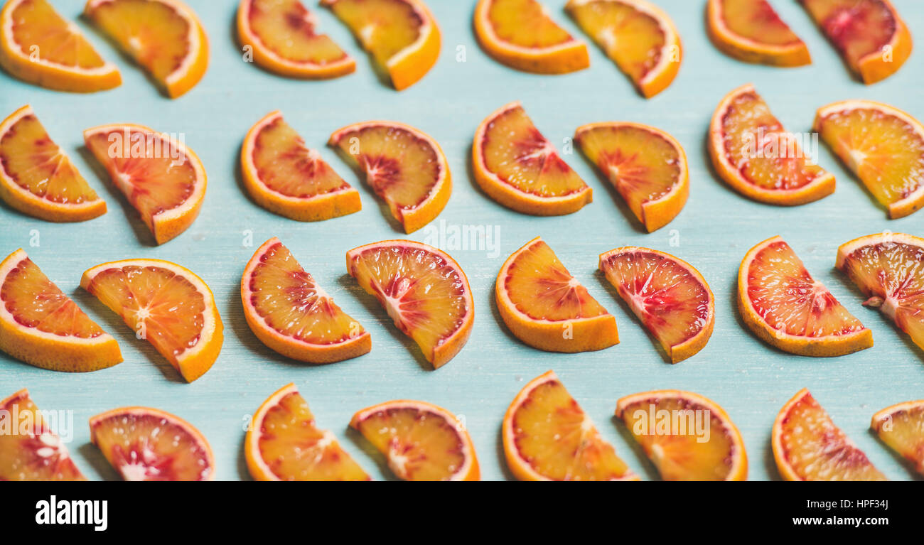 Natural fruit pattern concept. Fresh juicy blood orange slices placed in rows over light blue painted table background, selective focus Stock Photo