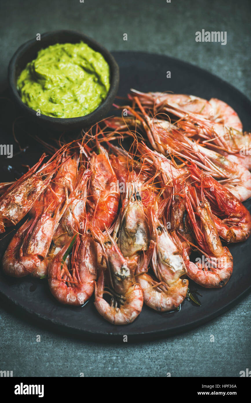 Roasted red shrimps with guacamole avocado sauce in slate stone black plate over grey concrete background, selective focus Stock Photo