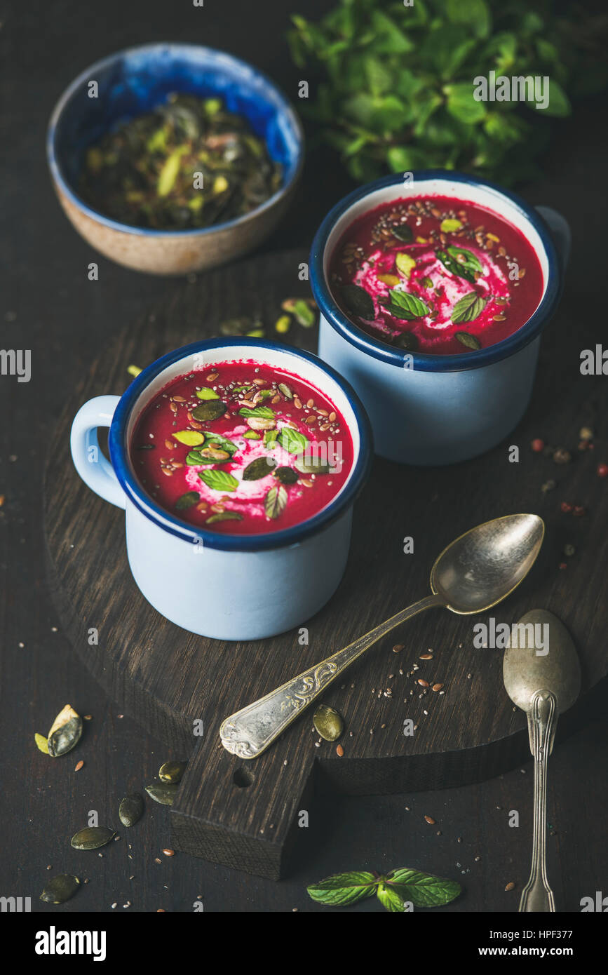 Spring detox beetroot soup with mint, pistachio, chia, flax and pumpkin seeds in blue enamel mugs over dark wooden background. Clean eating, healthy, Stock Photo