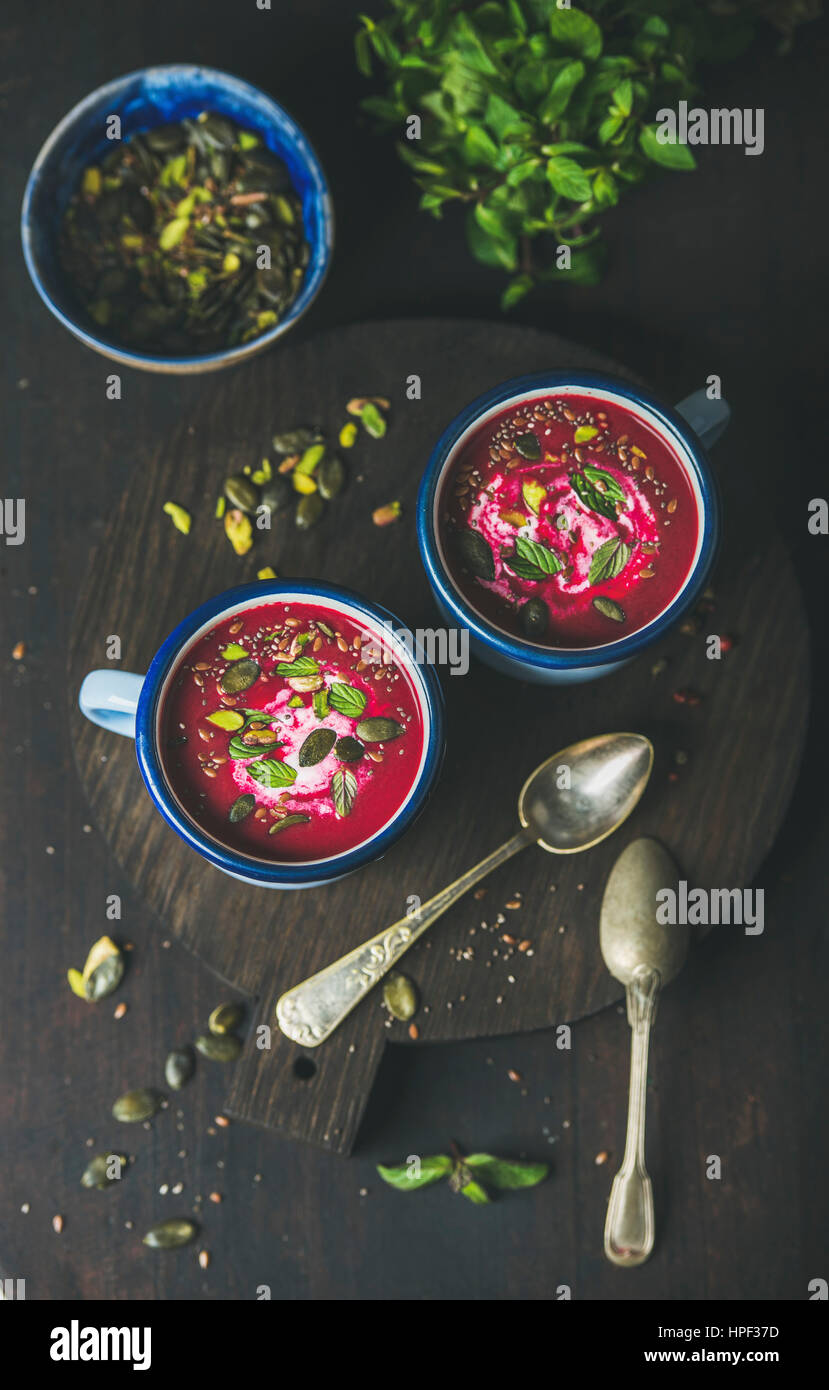 Spring beetroot soup with mint, pistachio, chia, flax, pumpkin seeds in blue enamel mugs over dark wooden background, top view. Clean eating, healthy, Stock Photo