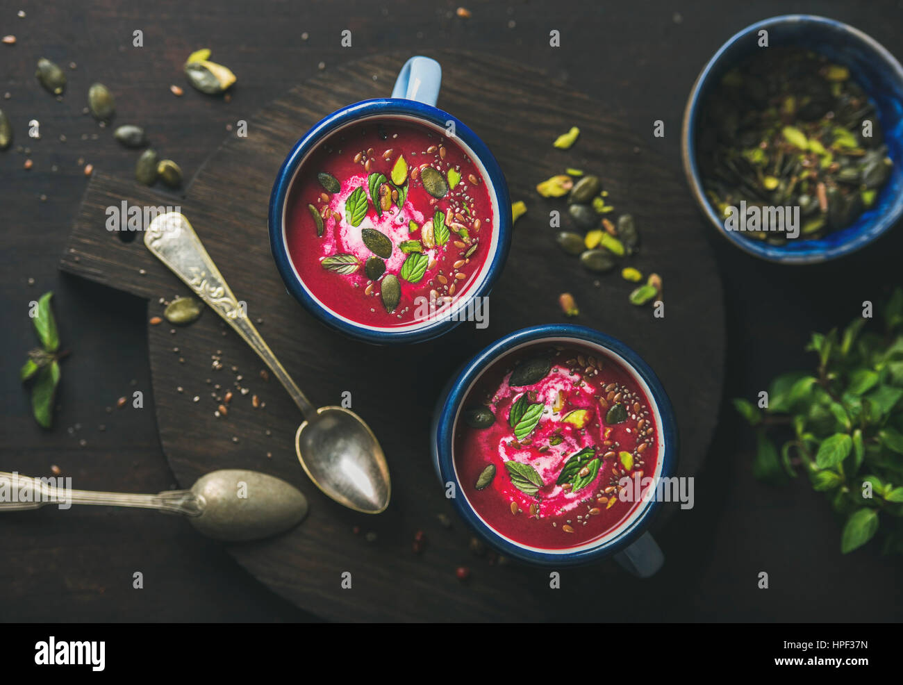 Spring detox beetroot soup with mint, pistachio, chia, flax and pumpkin seeds in blue enamel mugs over dark wooden background, top view. Clean eating, Stock Photo