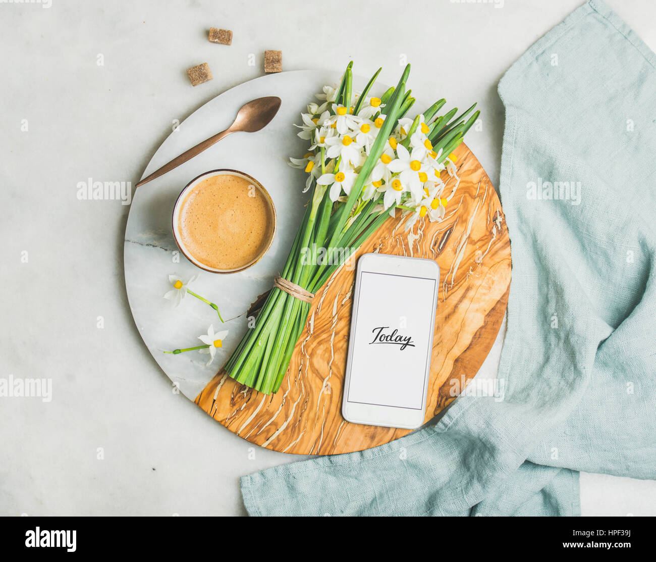Cup of morning coffee, bucket of spring flowers and mobile phone with text Today on serving board over light grey marble background, top view. Morning Stock Photo