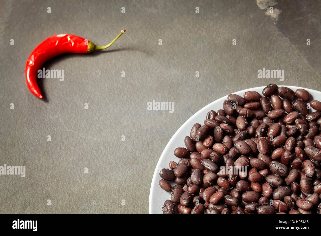 Black bean plate and red chili on slate background, selective focus, copy space. Stock Photo