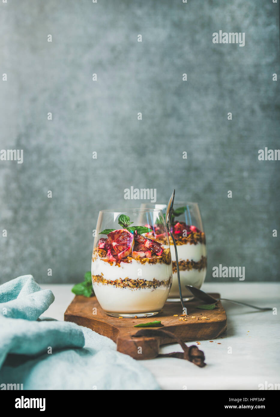 Healthy breakfast. Greek yogurt, granola, blood orange layered parfait in glasses with mint on wooden board, grey concrete wall at background, copy sp Stock Photo