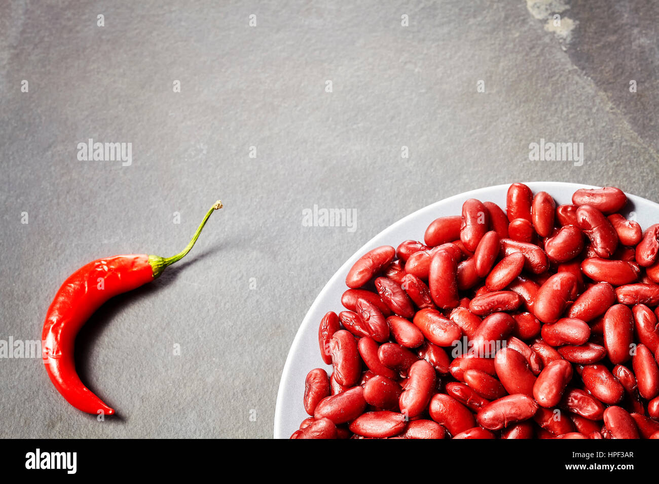Red kidney bean plate and red chili on slate background, selective focus, copy space. Stock Photo