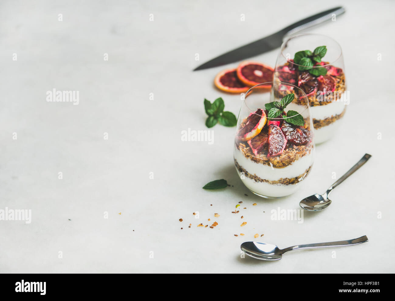 Healthy breakfast. Greek yogurt, granola and blood orange layered parfait in glasses with mint leaves over grey marble background, copy space. Clean e Stock Photo