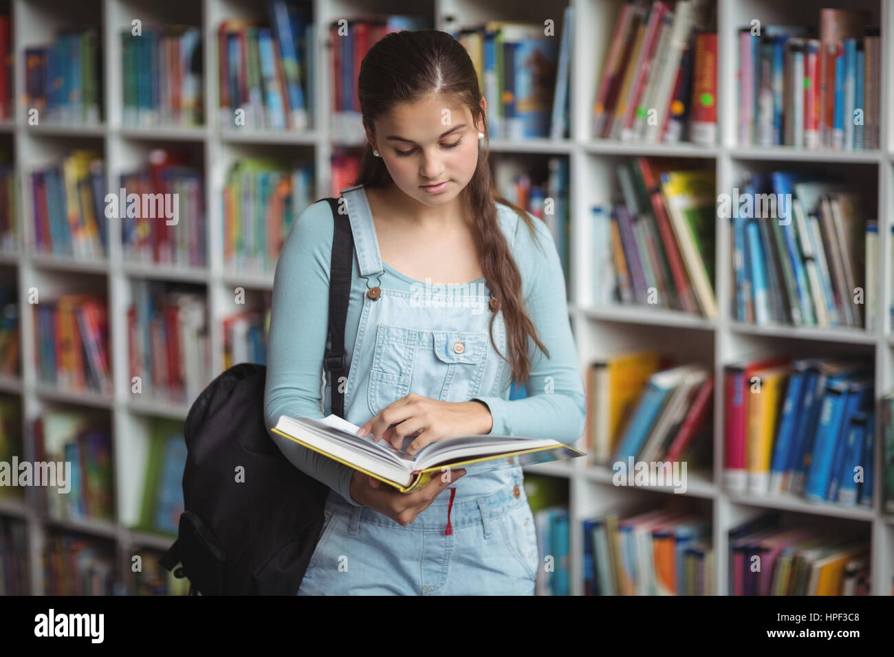 Attentive schoolgirl reading book in library at school Stock Photo - Alamy