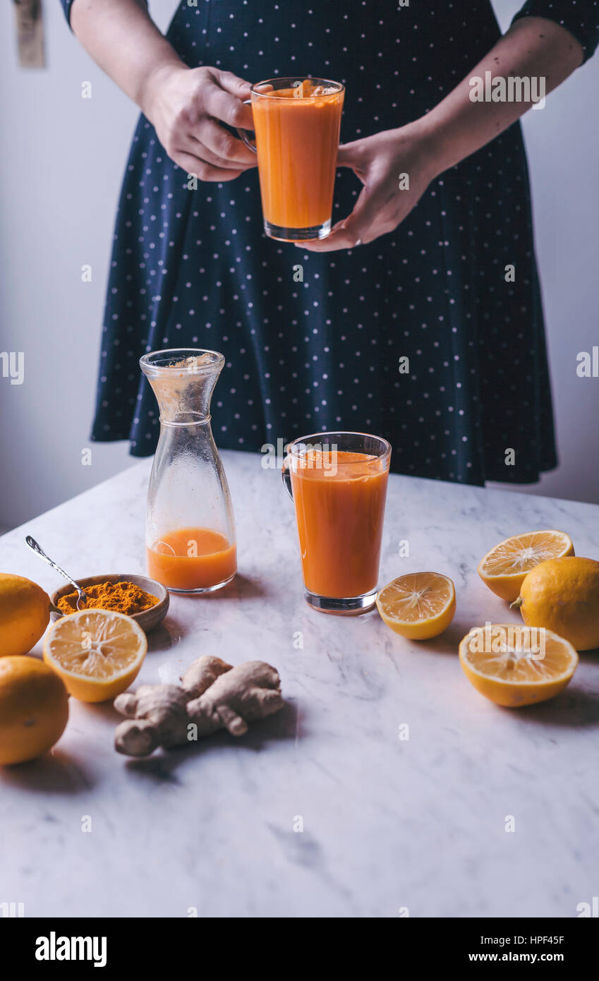 Woman holding a glass of orange lemon and carrot juice with turmeric