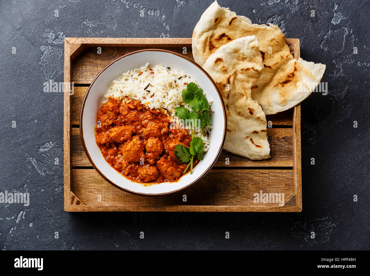 Chicken tikka masala spicy curry meat food with rice and fresh naan bread in wooden tray on black stone background Stock Photo