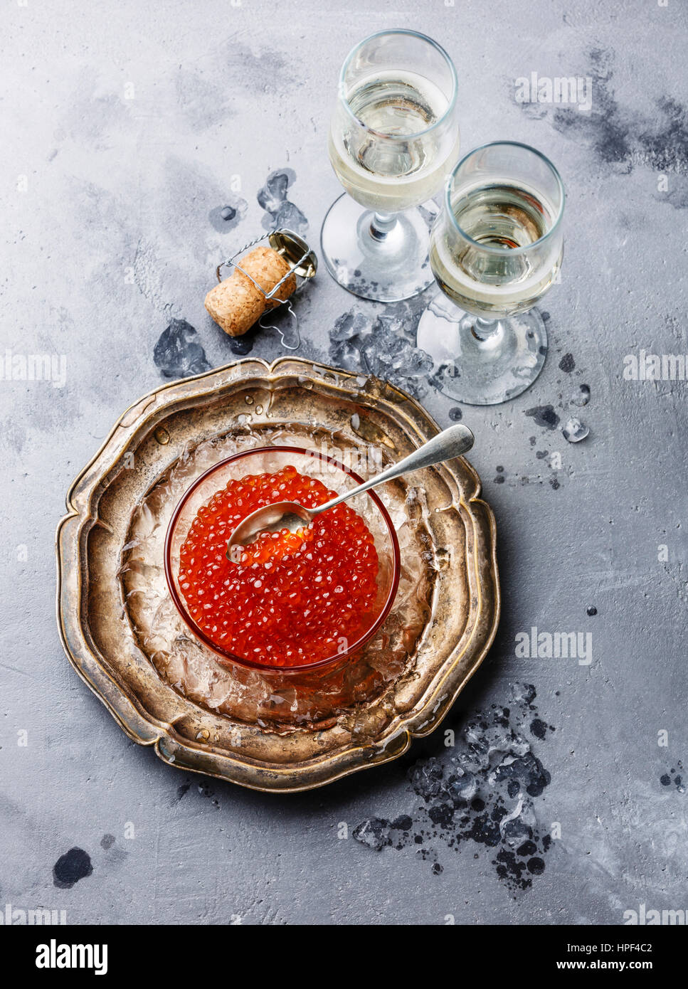Red caviar in glass bowl on ice and champagne on concrete background Stock Photo