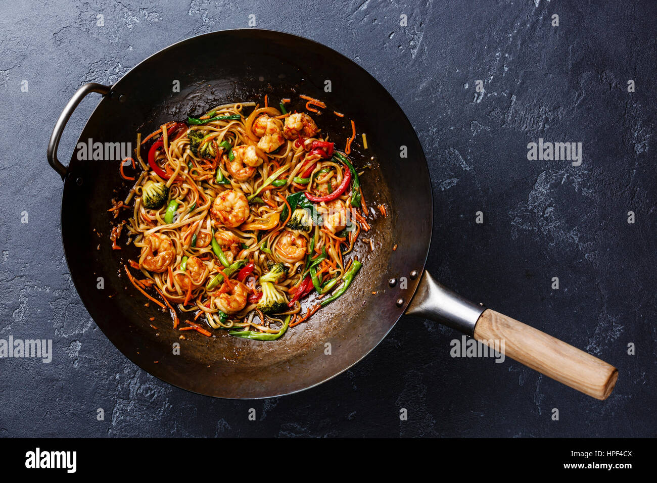 Udon stir-fry noodles with shrimp in wok pan on dark stone background Stock Photo