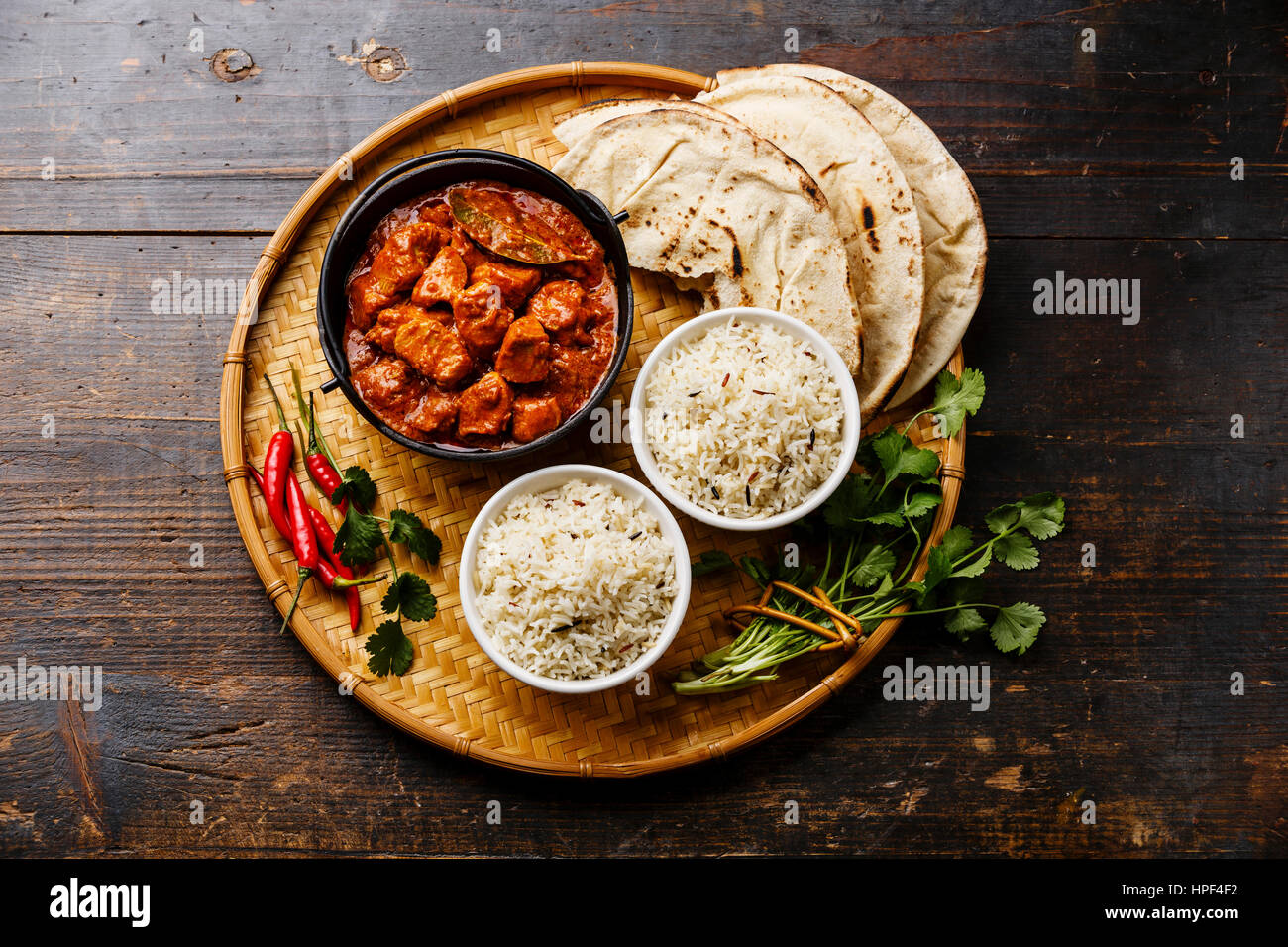 Chicken tikka masala spicy curry meat food in cast iron pot with rice and naan bread on wooden background Stock Photo
