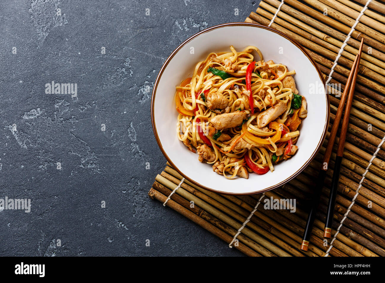 Udon stir-fry noodles with chicken in bowl on dark stone background copy space Stock Photo