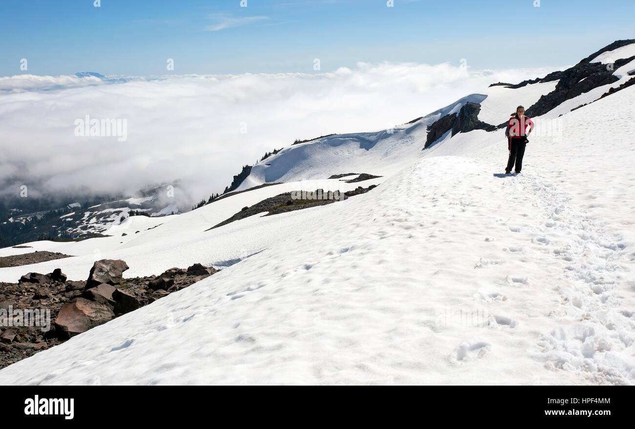A female hiker adventuring above the clouds on a snowy mountain trek. Taken at Mount Rainer National Park in Washington state. Stock Photo