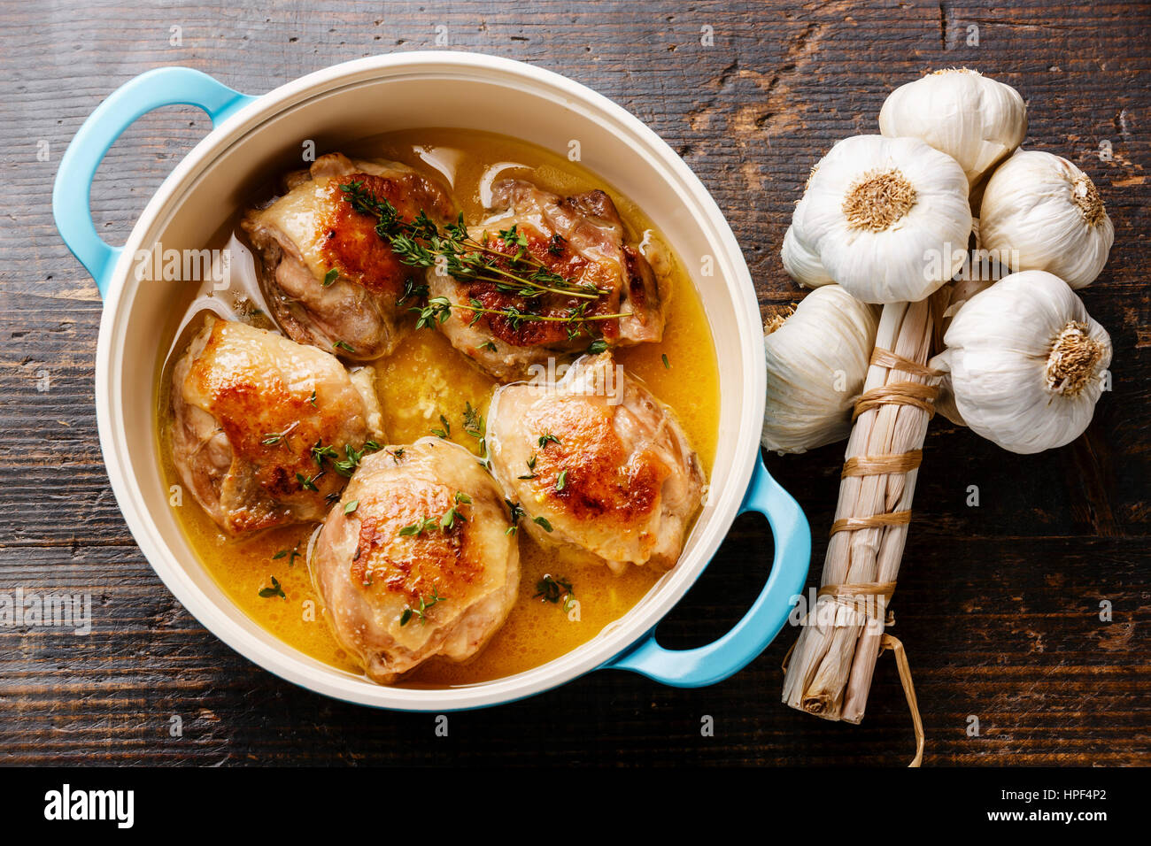 Roast chicken stew in casserole and garlic on wooden background Stock Photo