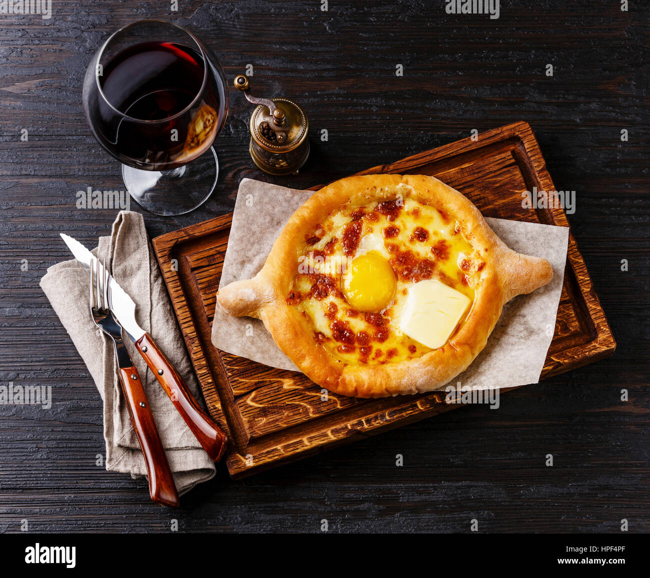 Ajarian Khachapuri traditional Georgian cheese pastry and wine on burned black wooden background Stock Photo