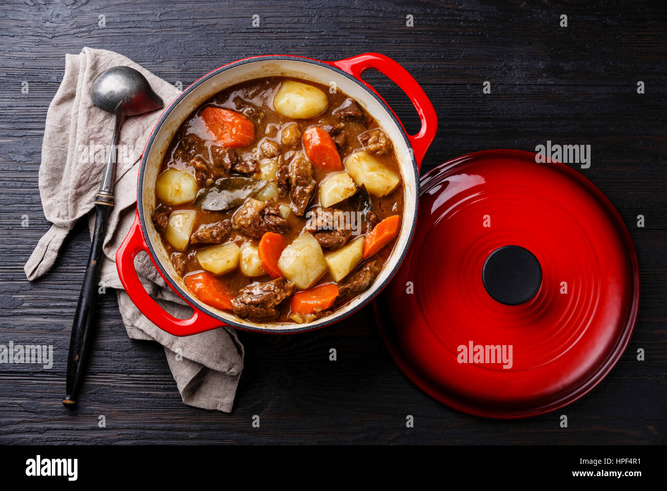 Beef meat stew pot with potatoes, carrots and spices in cast iron pan on burned black wooden background Stock Photo