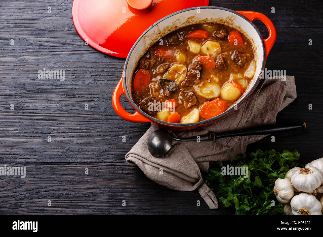 Beef meat stew with potatoes, carrots and spices in cast iron pot on burned black wooden background copy space Stock Photo