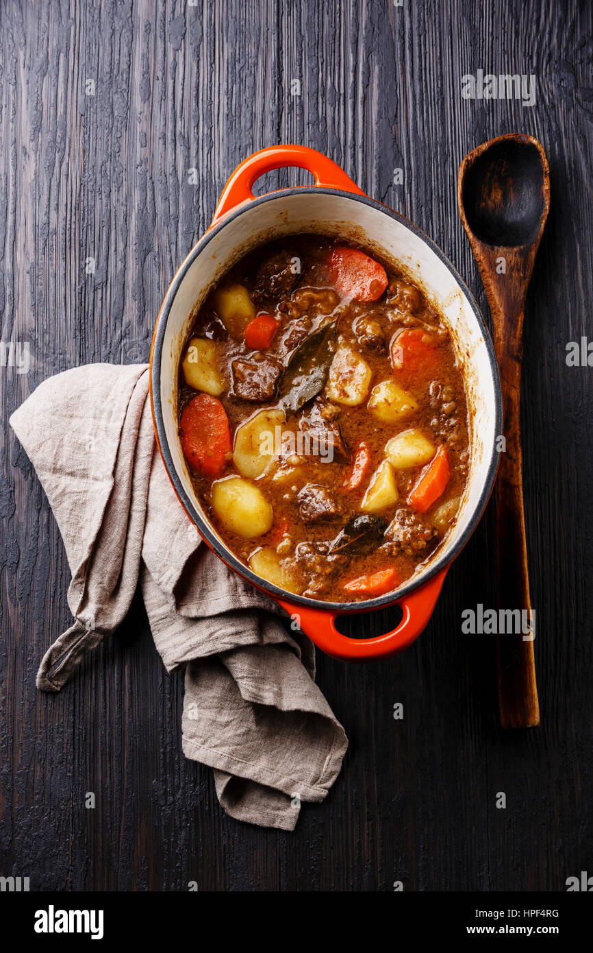 Beef meat stew with potatoes, carrots and spices in cast iron pot on burned black wooden background Stock Photo