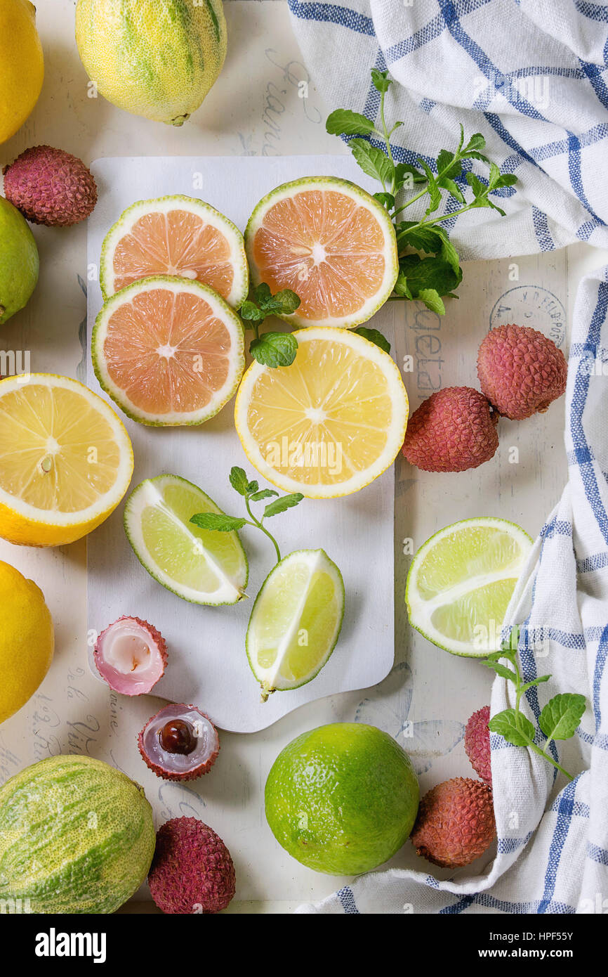 Variety of whole and sliced citrus fruits pink tiger lemon, lemon, lime, mint and exotic lichee on white chopping board with kitchen towel over white Stock Photo