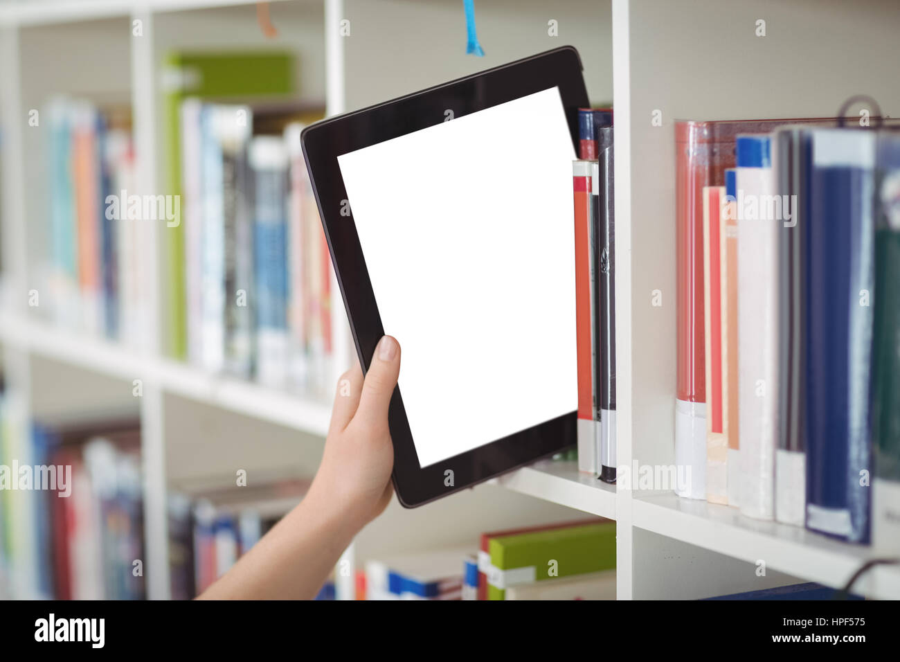 Hand of student keeping digital tablet in bookshelf in library at