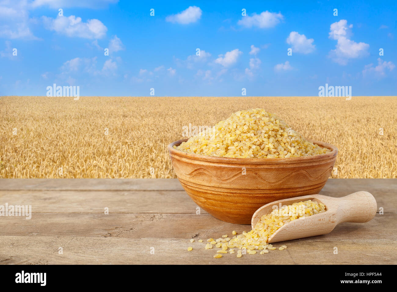 Bulgur or couscous in bowl. wheat grains in sack. Bulgur in ceramic bowl on table with field of wheat on the background. Agriculture and harvest conce Stock Photo