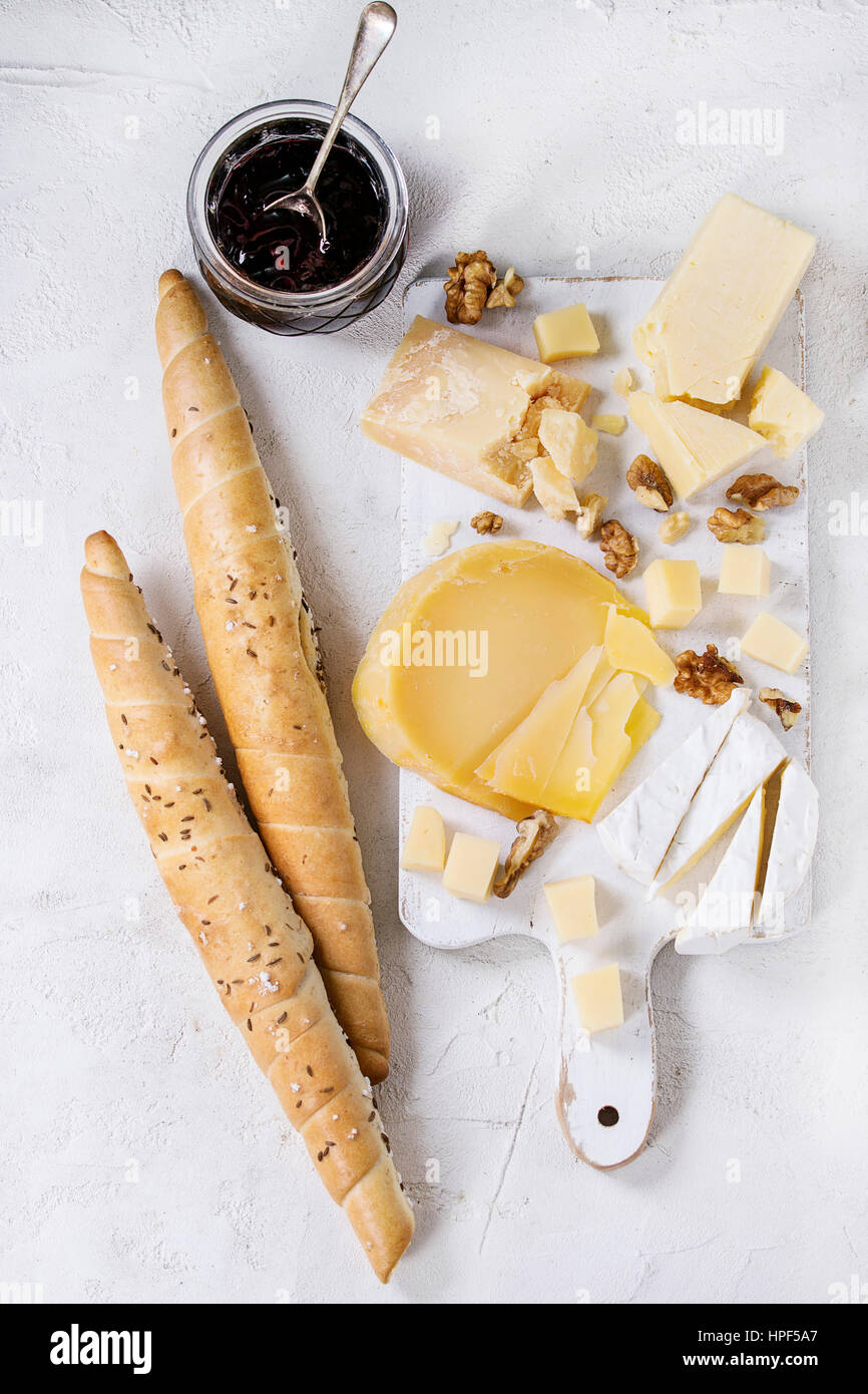 Cheese plate. Assortment of cheese with walnuts, jam and bread on white wood serving board over white concrete texture background. Top view with space Stock Photo