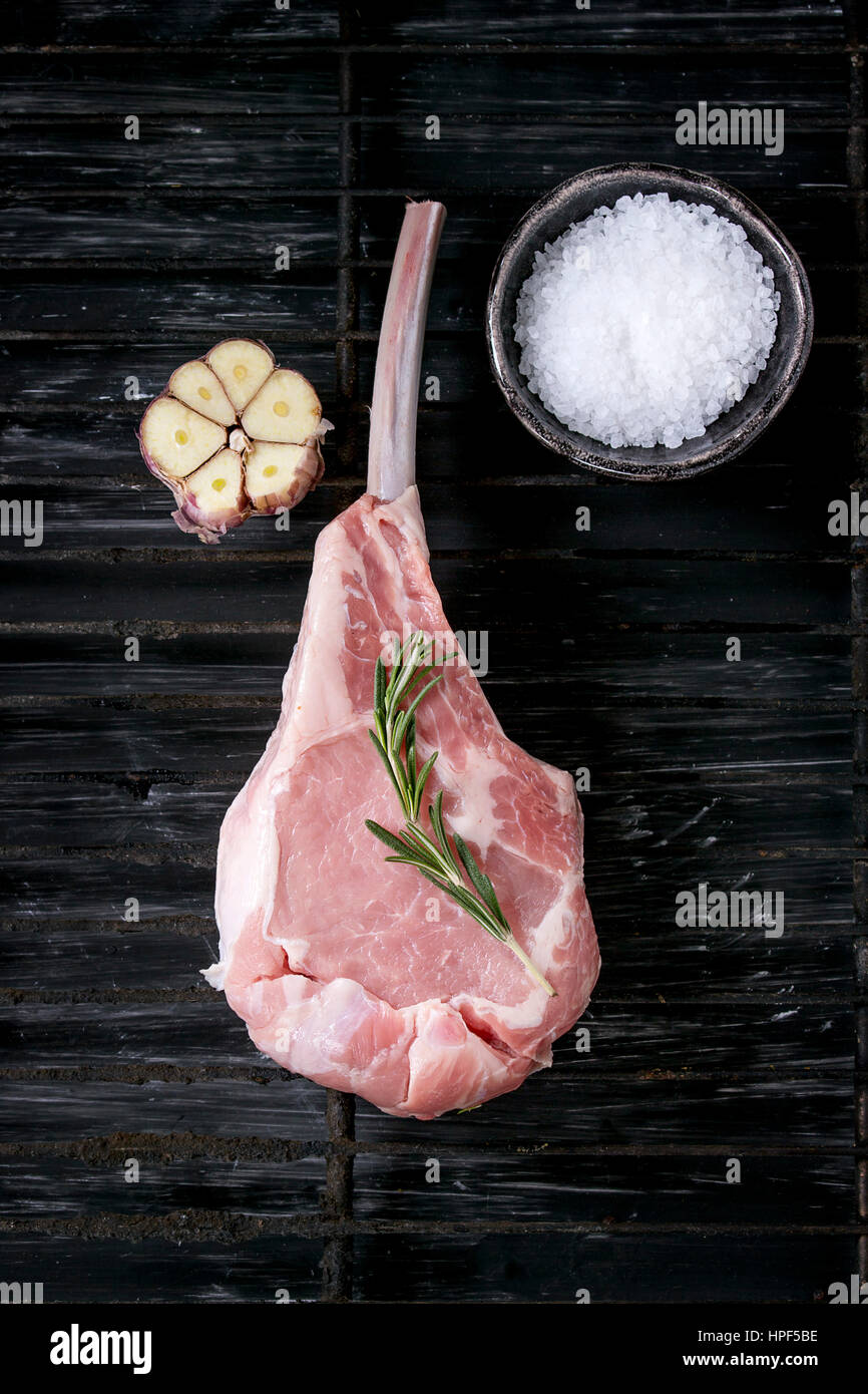 Raw uncooked Veal tomahawk steak with garlic, salt and seasoning on old grill grate over black texture background. Top view with space. Stock Photo