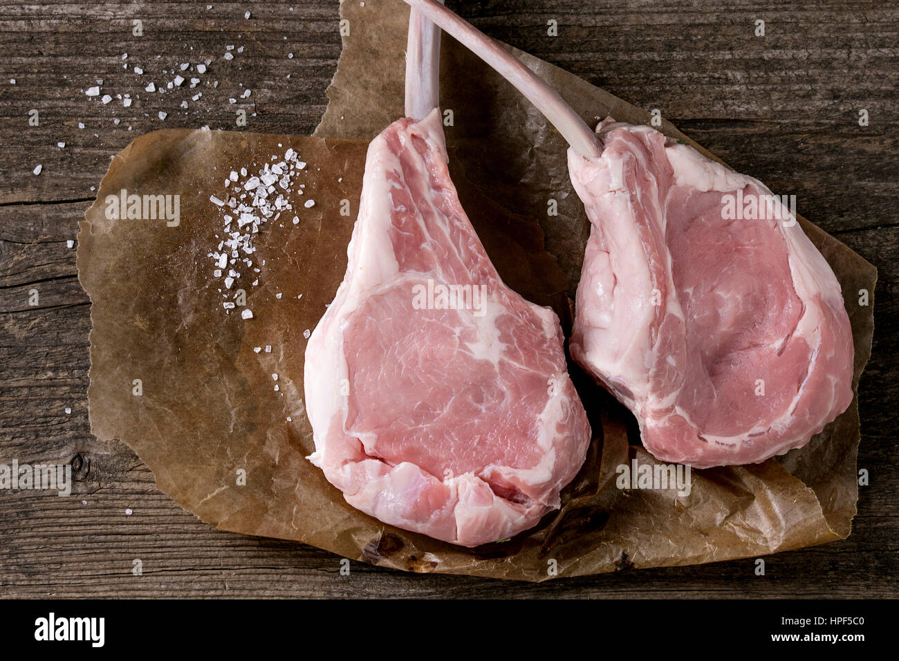 Two raw uncooked Veal tomahawk steak with sea salt on baking paper over old wooden background. Top view with space. Stock Photo