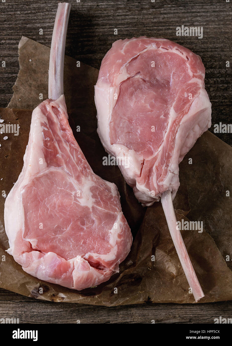 Two raw uncooked Veal tomahawk steak with sea salt on baking paper over old wooden background. Top view with space. Stock Photo