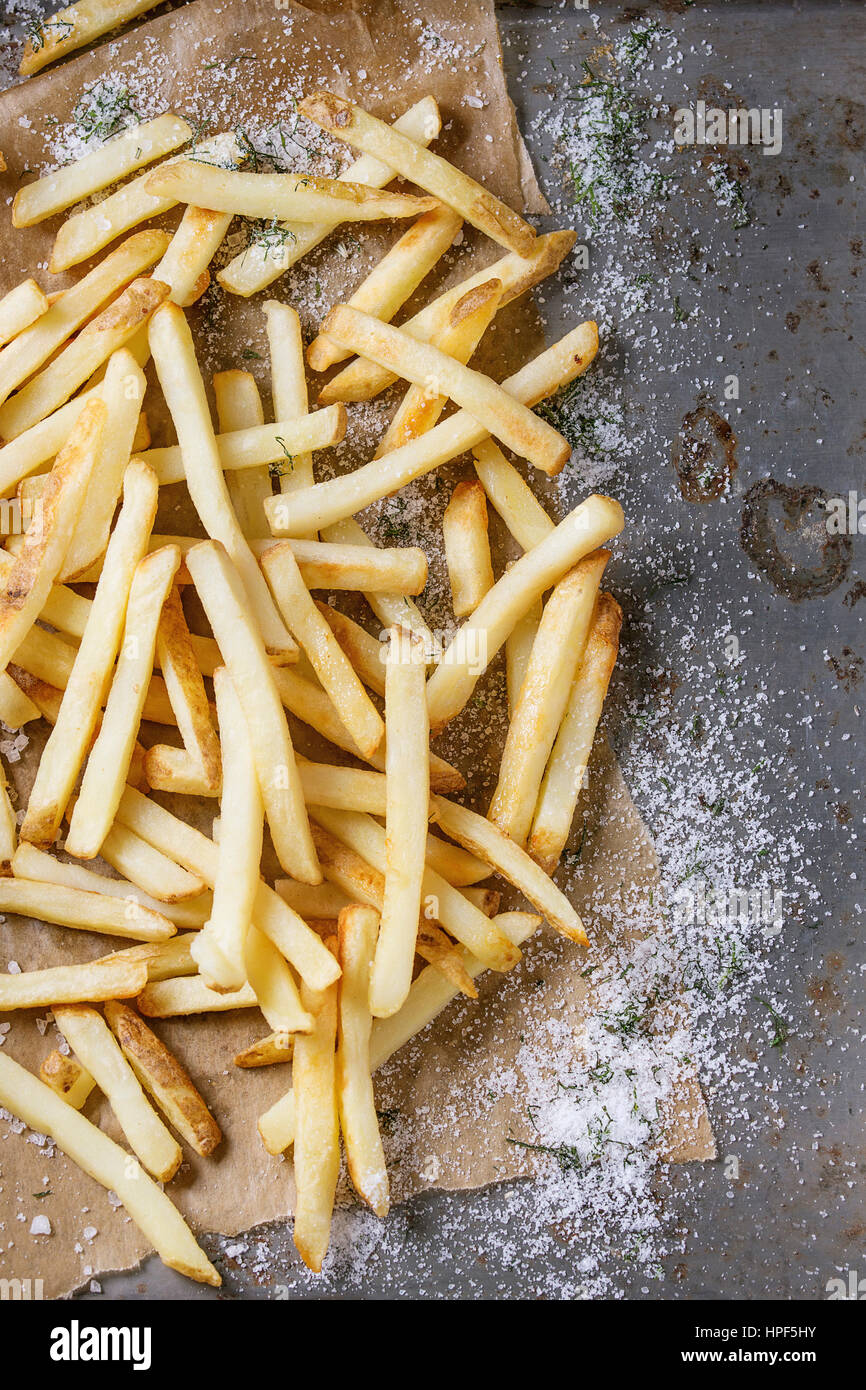 Fast food french fries potatoes with skin served with salt and herbs on baking paper over old rusty metal background. Top view, space for text Stock Photo