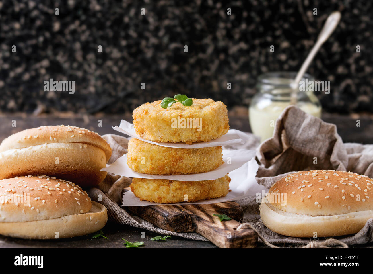 Ingredients for making vegan burger. Veggie cheese and onion cutlets, yogurt sauce, hamburger bunsand  herbs , served on wooden board with textile on Stock Photo