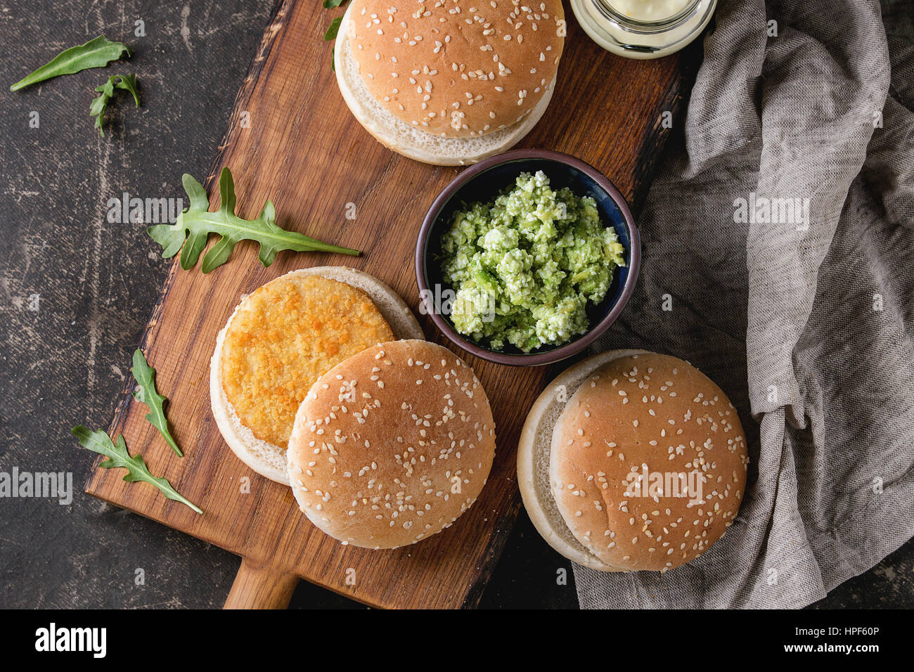 Ingredients for making vegan burger. Veggie cheese and onion cutlets, yogurt sauce, hamburger buns, herbs and avocado salad, served on wooden board wi Stock Photo
