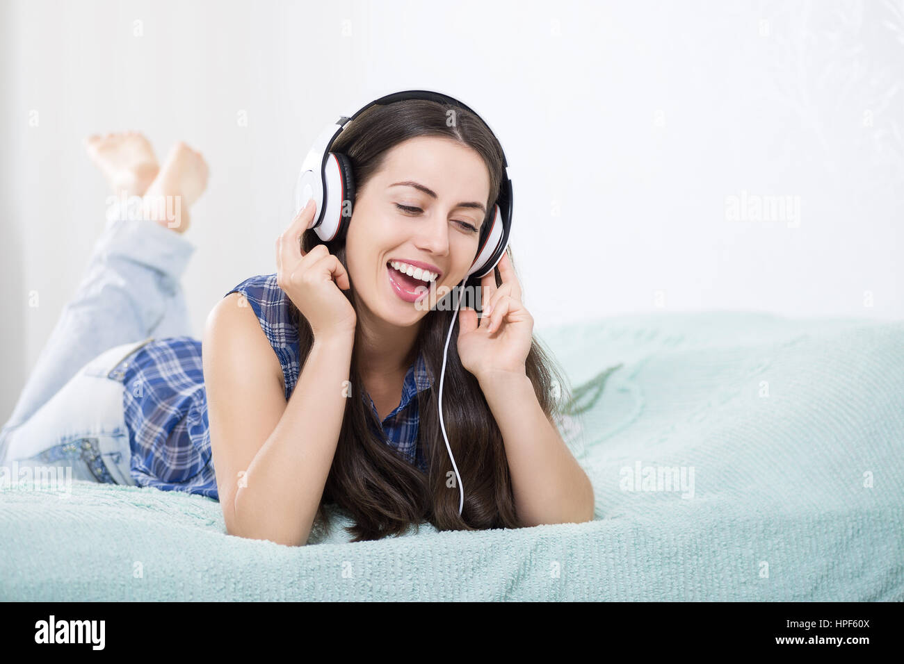 Happy girl listening music using headphones and singing on bed at home. People, leisure and technology concept - happy woman or teenage girl Stock Photo