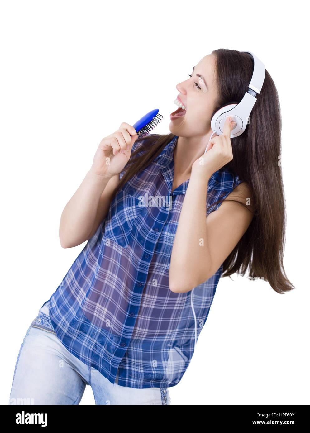 girl in headphones singing with her hairbrush as microphone isolated on white. Playful woman listening to music playing through her headphones and pre Stock Photo