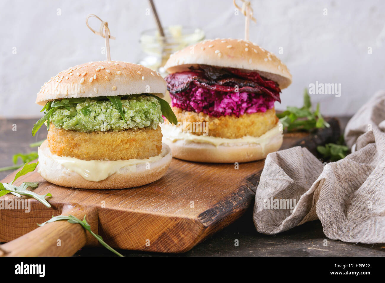 Two vegetarian hamburgers with onion and cheese cutlets, avocado salad, arugula, fried beetroot and yogurt sauce on wooden serving board over texture Stock Photo