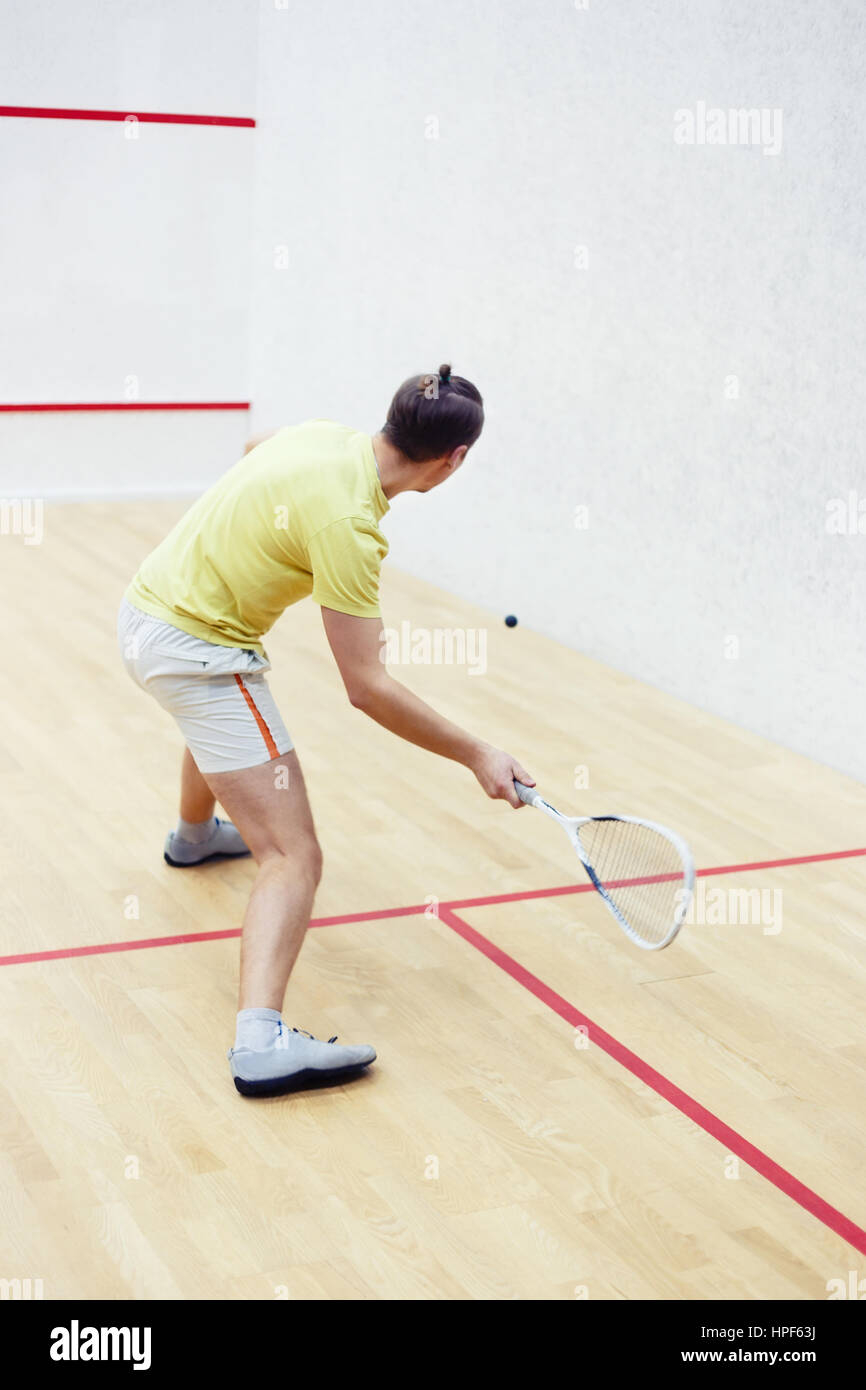 Back view of squash player in action reaching on squash court. Squash