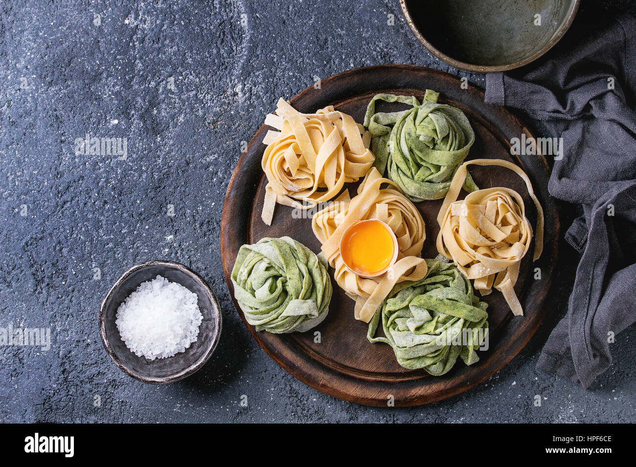 Variety of raw uncooked homemade pasta tagliatelle green spinach and traditional yellow with egg yolk ready to cook with salt on wood cutting board ov Stock Photo