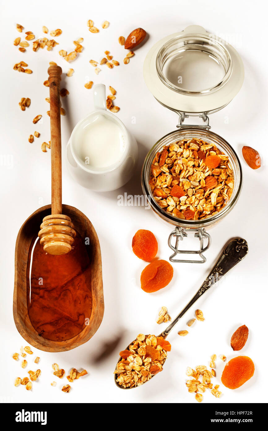 Homemade granola (with dried fruit and nuts) and healthy breakfast ingredients - honey, milk and fruits on white background Stock Photo