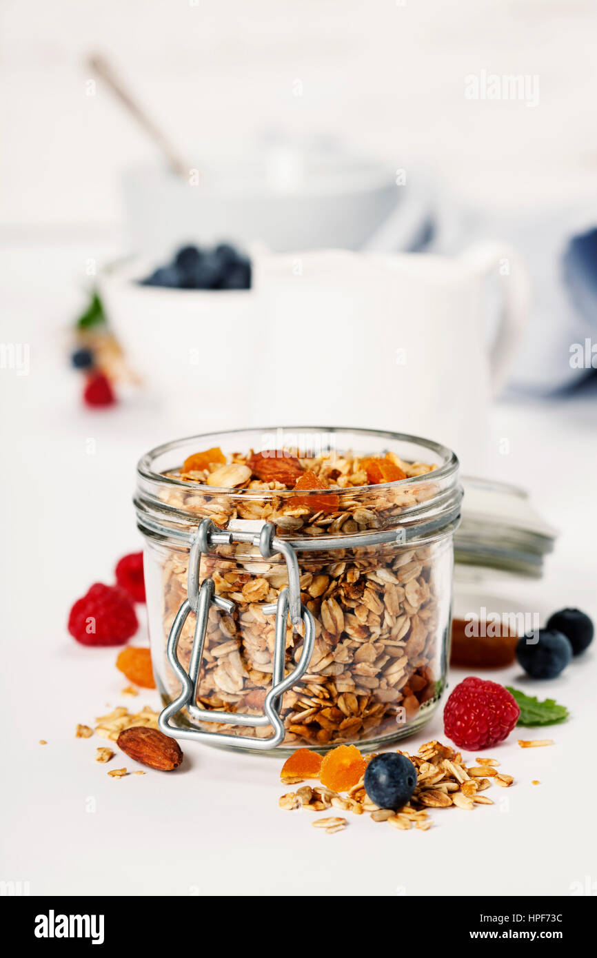 Homemade granola (with dried fruit and nuts) and healthy breakfast ingredients - honey, milk and berries on white background Stock Photo