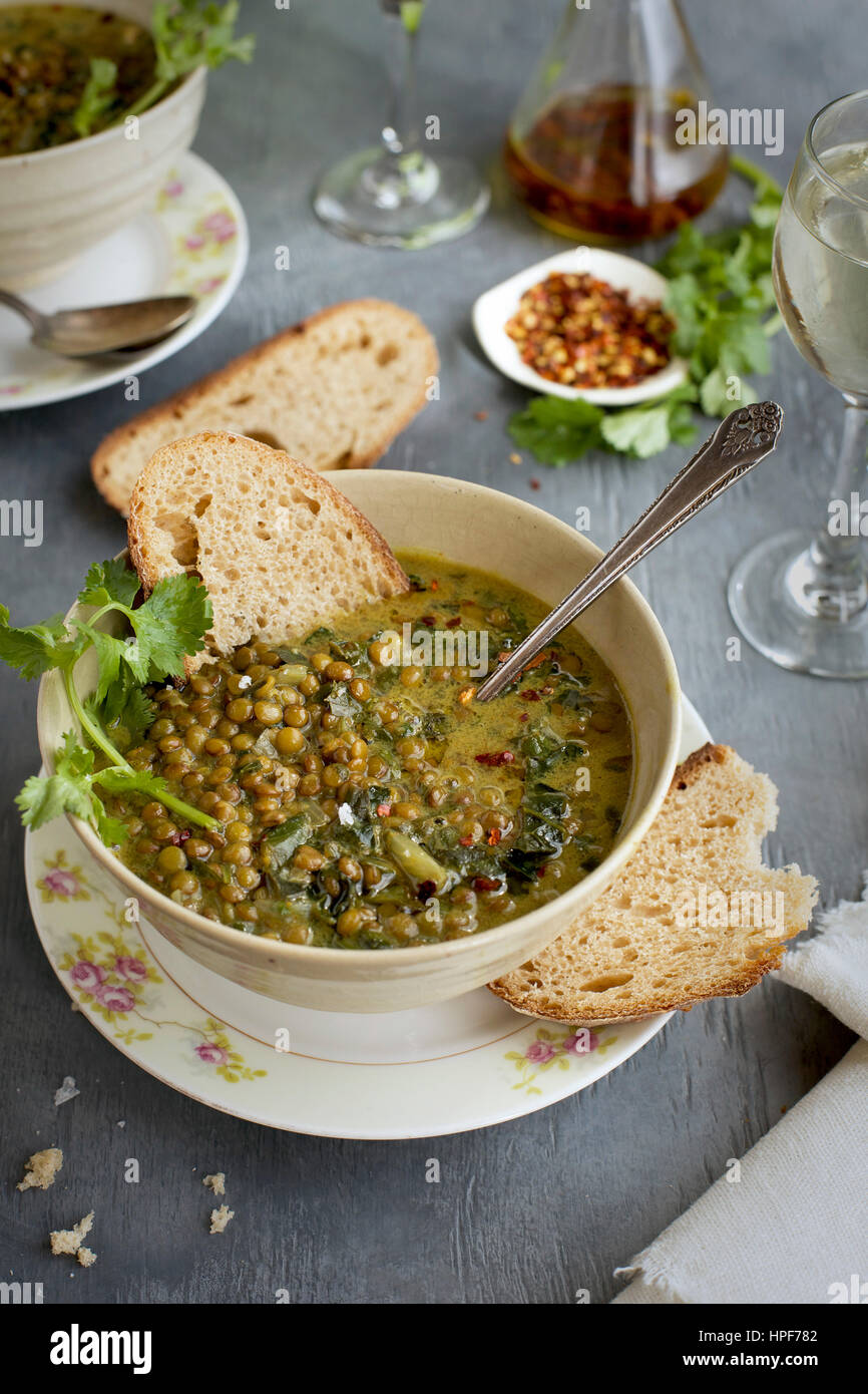 Green Lentil Coconut Soup in ceramic bowls served with bread and white wine.  Photographed on a gray background. Stock Photo