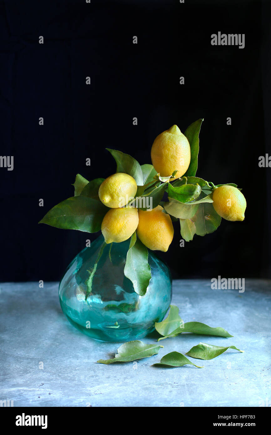 Lemons on a twig with green leaves in a glass vase on a table Stock Photo
