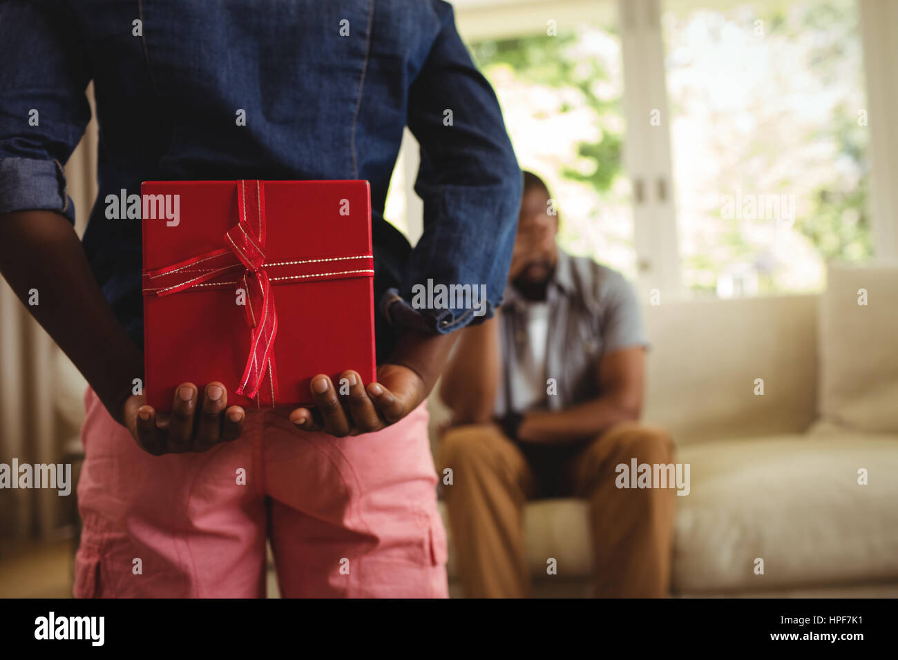 Son hiding gift behind his back for father at home Stock Photo