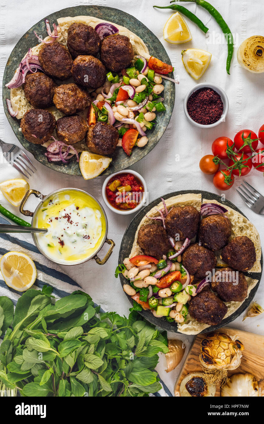 Turkish meatballs aka koftes served on pita bread on two copper plates with cold bean salad and red onions photographed from top view. Yogurt sauce, h Stock Photo