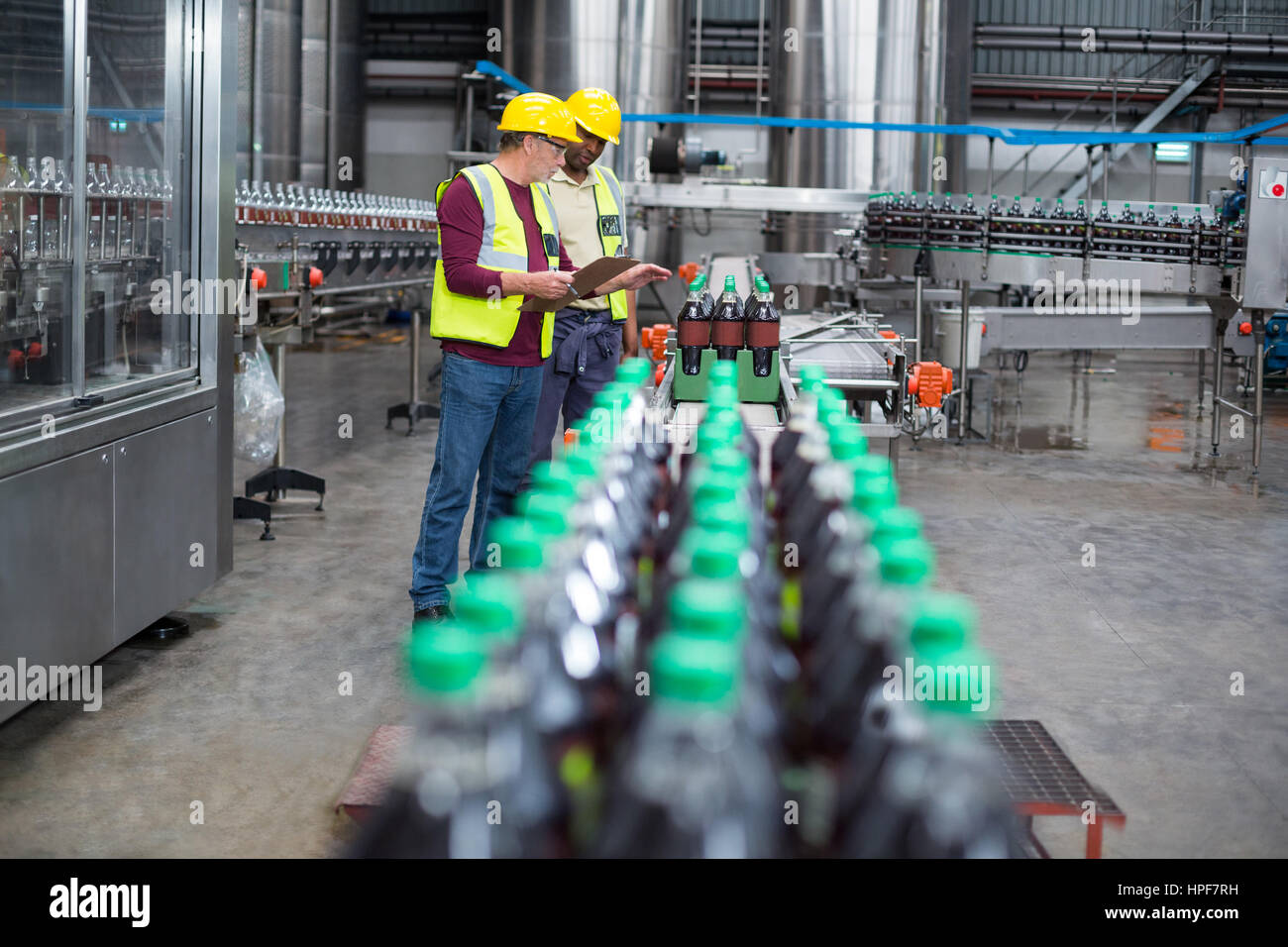 Two factory workers monitoring cold drink bottles on production line at